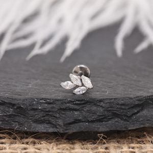 May include: A silver-toned ear piercing stud featuring a cluster of four marquise-cut, clear gemstones. The stud has a flat back and a small, round post for insertion. The gemstones are arranged in a leaf-like pattern.