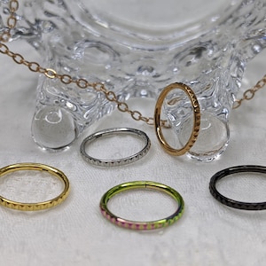 Puede incluir: Cinco anillos circulares de diferentes colores y texturas con un borde texturizado. Los anillos son de metal y están dispuestos sobre una superficie blanca.