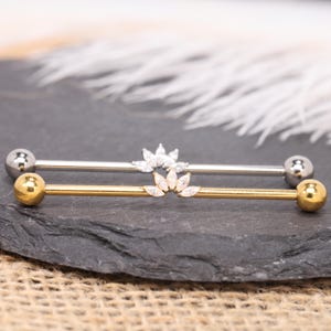 May include: Two industrial barbell piercings with spherical end caps. One barbell is silver-toned with a clear crystal fan-shaped accent, and the other is gold-toned with a matching clear crystal fan-shaped accent at the center.