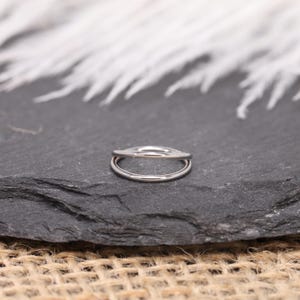 May include: A silver-colored double-band ring. The ring has a smooth, polished finish and a minimalist design. The ring is set against a dark gray, textured surface.