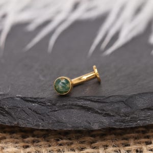 May include: A gold-coloured, flat-back earring featuring a round, green stone. The earring has a straight post and a small, flat disc at the back. The stone has a mottled appearance with shades of green.