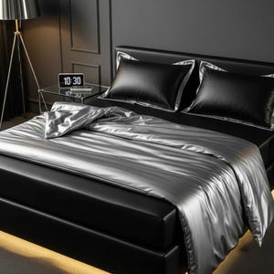 May include: A modern bed with black leather upholstery and a silver satin comforter. Two black pillows with silver trim are on the bed. A digital clock displays 10:30 on a glass side table.