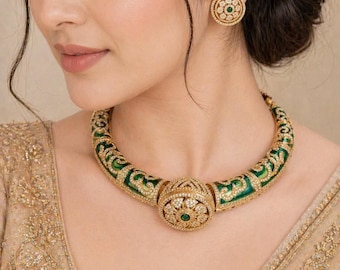Op de afbeelding: Een gouden ketting en bijpassende oorbellen set. De ketting heeft een groen emaille ontwerp met gouden accenten en is versierd met heldere edelstenen. De oorbellen zijn cirkelvormig met een vergelijkbaar edelsteen- en emaille ontwerp.