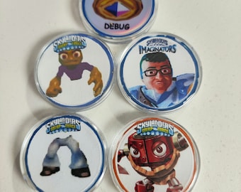May include: Five round Skylanders Swap Force character tokens. The tokens are clear plastic with a white background and a colourful image of a character. The tokens include a purple character, a blue character, a pair of blue jeans, a red robot, and a token that says "DEBUG".