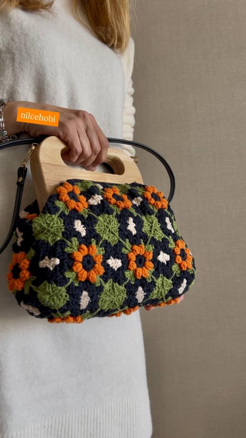 Puede incluir: Bolso de mano de ganchillo con asa de madera. El bolso presenta un estampado floral en naranja, verde, blanco y azul marino. El texto "nilcehobi" es visible en la imagen.