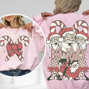 May include: Pink sweatshirt with a Christmas-themed design featuring Santa Claus and candy canes. The text "Metal Jolly" is printed on the sweatshirt.