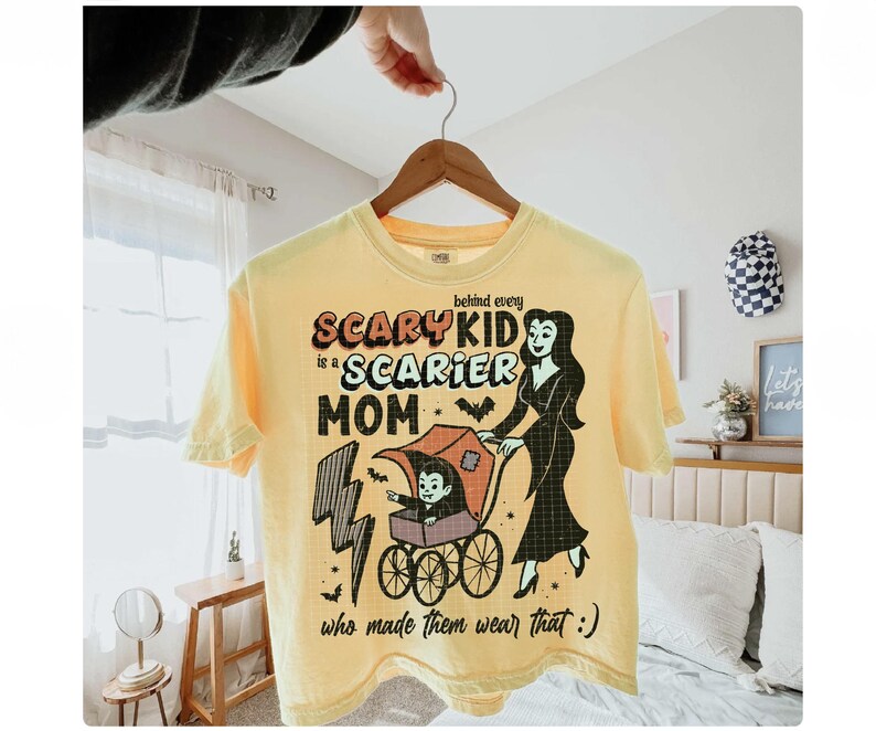 May include: Yellow t-shirt with the text "Behind every scary kid is a scarier mom who made them wear that :)". The graphic features a vampire mom pushing a stroller with a vampire child.