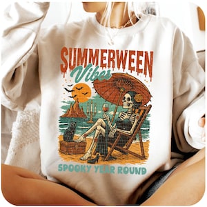 May include: White sweatshirt with a colorful graphic. The graphic features a skeleton relaxing on a beach chair under an umbrella, holding a glass of wine. Text reads "SUMMERWEEN Vibes" and "SPOOKY YEAR ROUND".