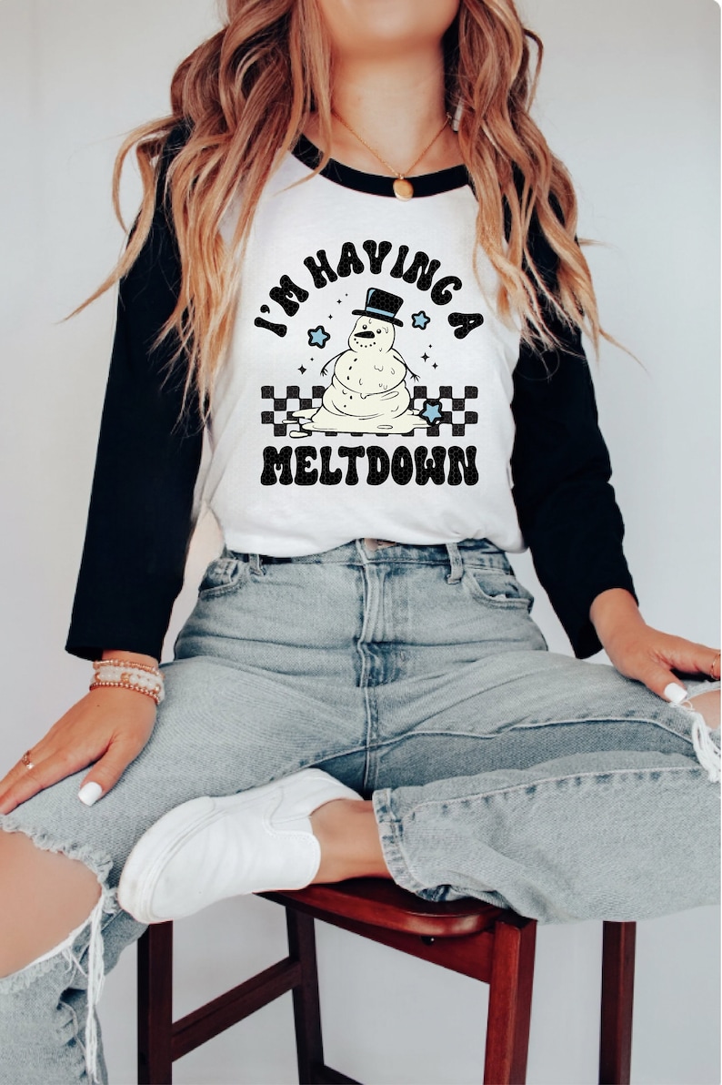 Pu&ograve; includere: Una maglietta da baseball bianca e nera con un grafico di pupazzo di neve che si scioglie e il testo "I'm having a meltdown".