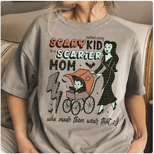 May include: Gray t-shirt with a Halloween-themed graphic. The design features the text "Scary Kid is a Scarier Mom" with a cartoon illustration of a vampire baby in a stroller being pushed by a woman in a black dress.
