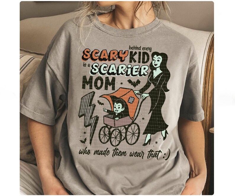 May include: Gray t-shirt with a Halloween-themed graphic. The design features the text "Scary Kid is a Scarier Mom" with a cartoon illustration of a vampire baby in a stroller being pushed by a woman in a black dress.