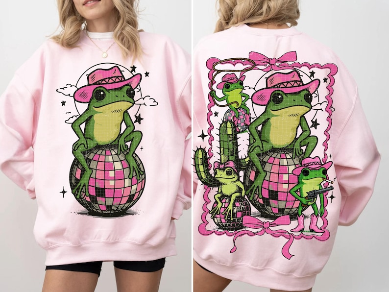 May include: Light pink sweatshirt featuring a green frog wearing a pink cowboy hat, sitting on a pink and silver disco ball. The back of the sweatshirt has a similar design with additional frogs, a cactus, and a pink frame.