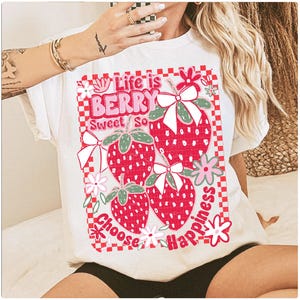 May include: White t-shirt with a graphic of strawberries and the text "Life is Berry Sweet So Choose Happiness".