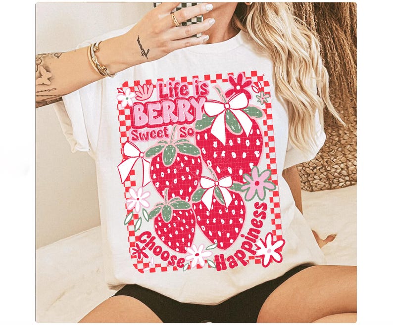 May include: White t-shirt with a graphic of strawberries and the text "Life is Berry Sweet So Choose Happiness".