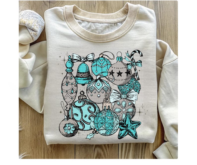 Peut inclure: Un sweat-shirt cr&egrave;me avec un imprim&eacute; graphique d'ornements de No&euml;l bleu sarcelle et argent. Les ornements sont dessin&eacute;s dans un style vintage et comprennent des cloches, des &eacute;toiles et des cannes en sucre.