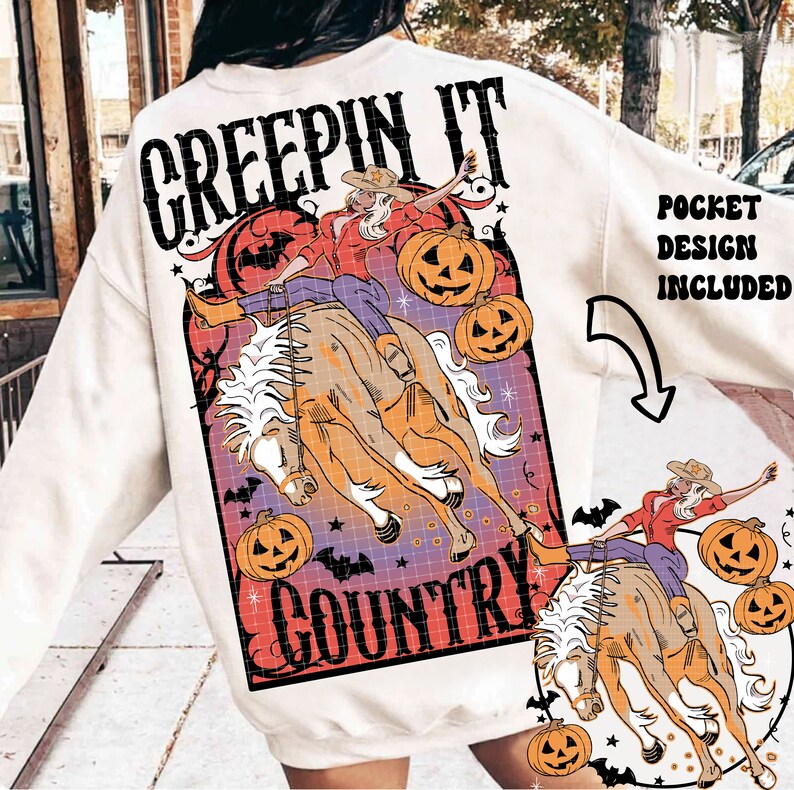 Puede incluir: Sudadera blanca con un estampado gr&aacute;fico de una mujer montando un caballo con el texto "Creepin' It Country". El gr&aacute;fico tambi&eacute;n incluye calabazas y murci&eacute;lagos. La sudadera tiene un bolsillo en la parte delantera.