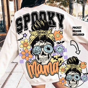 May include: White sweatshirt with a graphic print of a skull with a messy bun, wearing sunglasses and a headband. The text "Spooky Mama" is printed in orange and black. The text "Pocket Design Included" is printed in black on the right side of the sweatshirt.