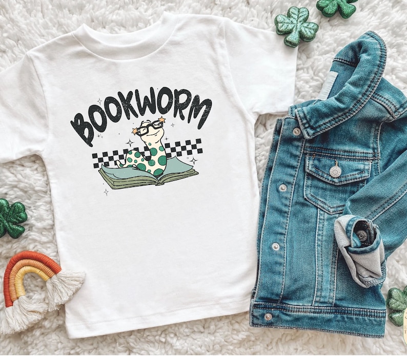Pu&ograve; includere: Maglietta bianca con un verme verde che indossa gli occhiali e legge un libro. La maglietta dice "BOOKWORM" in lettere nere.