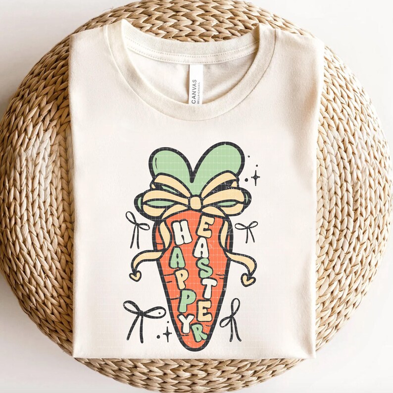 May include: A beige t-shirt with a graphic of a carrot with a bow on top. The carrot has the words "Happy Easter" written on it.