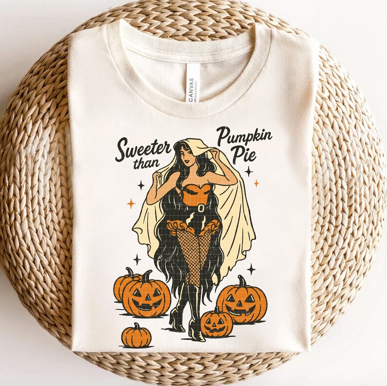 Peut inclure: T-shirt cr&egrave;me avec une illustration r&eacute;tro d'une femme en costume d'Halloween, entour&eacute;e de citrouilles sculpt&eacute;es. Le texte "Sweeter than Pumpkin Pie" est au-dessus de l'illustration. Le t-shirt est en mati&egrave;re douce.