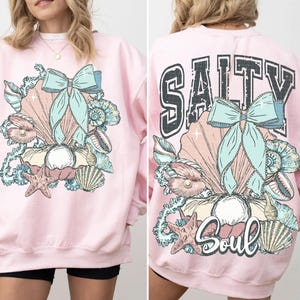 Puede incluir: Sudadera rosa con un dise&ntilde;o de concha y lazo en la parte delantera y el texto "Salty Soul" con un dise&ntilde;o de concha y lazo en la parte trasera.