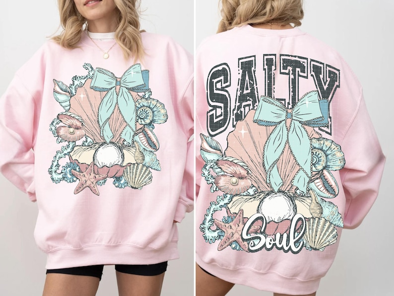 Puede incluir: Sudadera rosa con un dise&ntilde;o de concha y lazo en la parte delantera y el texto "Salty Soul" con un dise&ntilde;o de concha y lazo en la parte trasera.