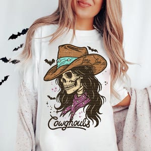 May include: White t-shirt featuring a skeleton wearing a cowboy hat with the text "Long Live" and a purple bandana. The design includes the text "Cowghouls" and bat silhouettes, perfect for Halloween.