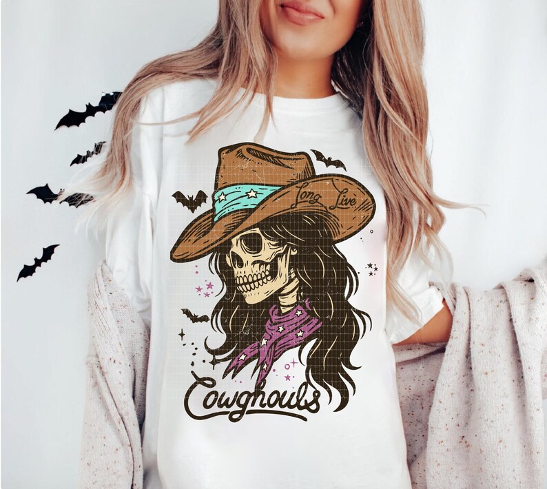 May include: White t-shirt featuring a skeleton wearing a cowboy hat with the text "Long Live" and a purple bandana. The design includes the text "Cowghouls" and bat silhouettes, perfect for Halloween.