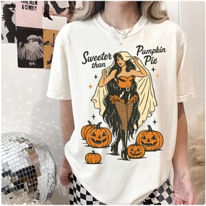 Peut inclure: T-shirt cr&egrave;me avec un motif sur le th&egrave;me d'Halloween. Le design pr&eacute;sente une femme costum&eacute;e, des citrouilles et le texte "Sweeter than Pumpkin Pie". Le t-shirt a une coupe ample.