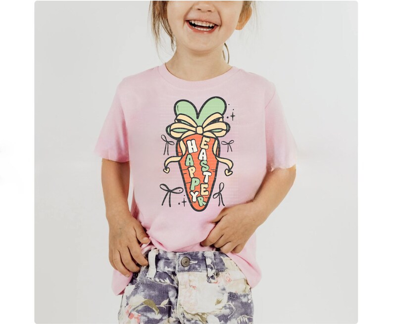May include: Pink short-sleeved t-shirt with a cartoon carrot graphic. The carrot has a green bow and the words "Happy Easter" written on it.