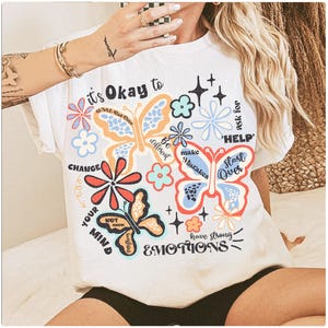 May include: White t-shirt with a colorful butterfly design and the text "It's Okay to Change Your Mind, Be Different, Make Mistakes, Ask for Help, Start Over, Have Strong Emotions".