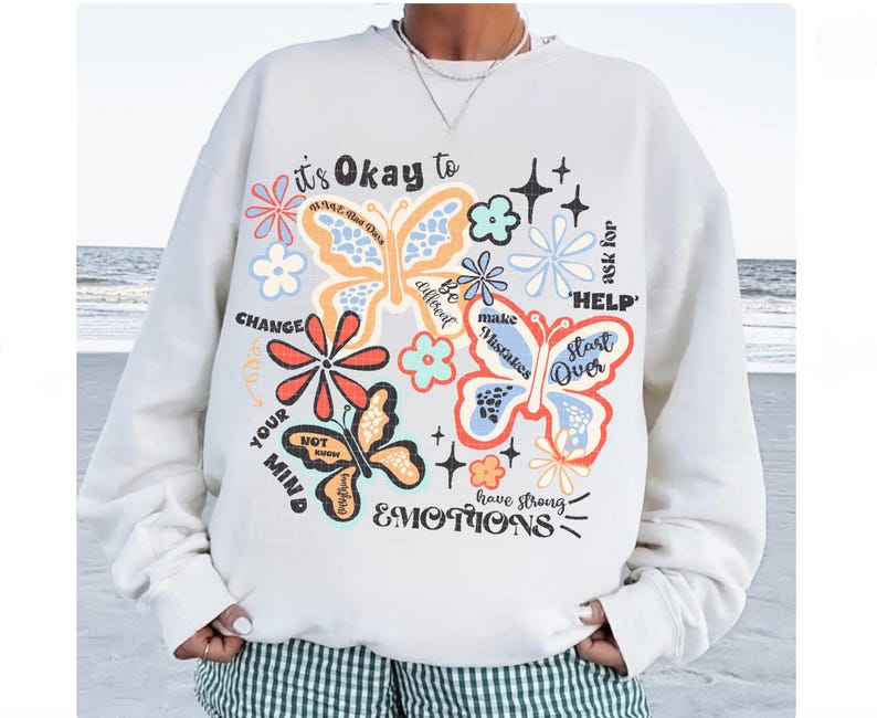 May include: White sweatshirt with a colorful butterfly graphic and the text "it's Okay to" and "ask for HELP". The graphic also includes flowers and the text "CHANGE YOUR MIND", "Be different", "make Mistakes", "Start Over", and "have strong EMOTIONS".