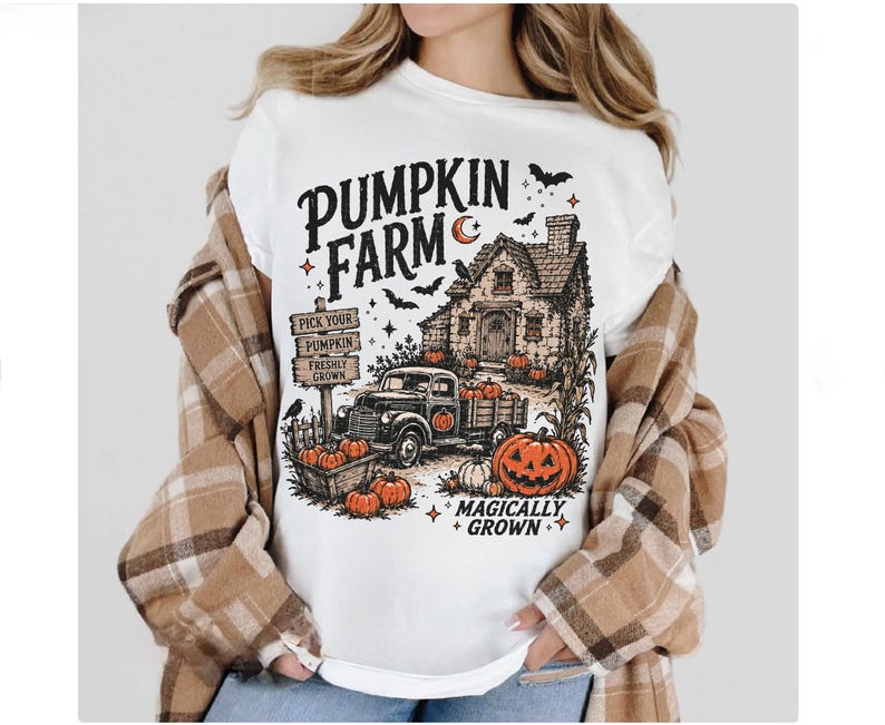 Peut inclure: Un t-shirt blanc avec une impression graphique repr&eacute;sentant une ferme de citrouilles, une maison, un camion et des citrouilles. Le texte indique PUMPKIN FARM et MAGICALLY GROWN, avec des panneaux PICK YOUR PUMPKIN FRESHLY GROWN. Le motif inclut des chauves-souris.