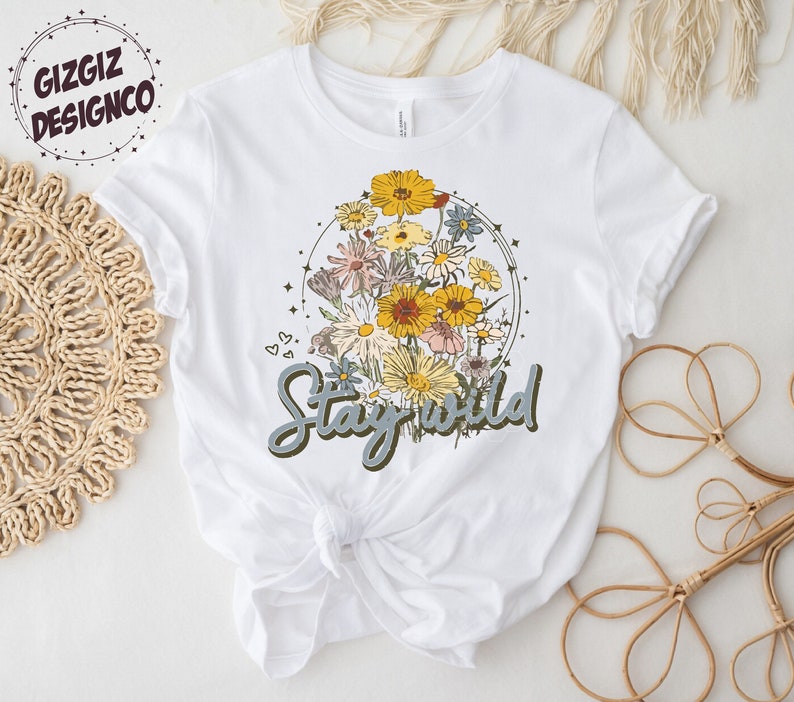 May include: White t-shirt with a floral design and the text "Stay Wild" in blue lettering.