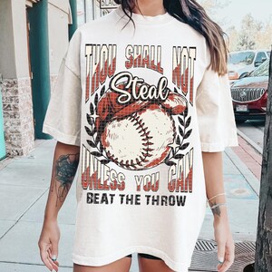 May include: White oversized t-shirt with a baseball graphic and the text "Thou Shall Not Steal Unless You Can Beat The Throw".