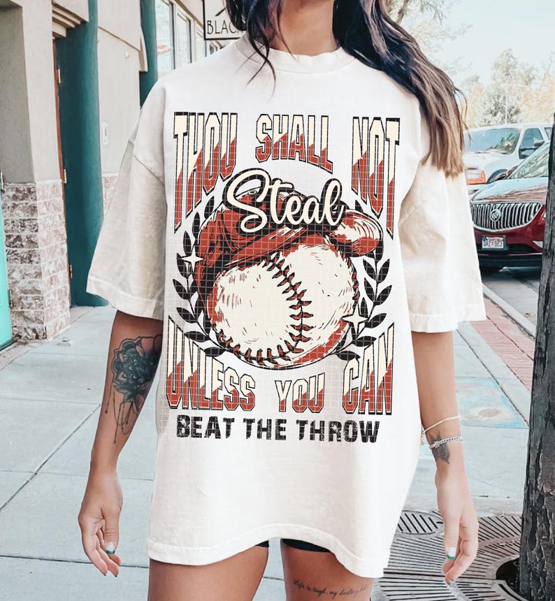 May include: White oversized t-shirt with a baseball graphic and the text "Thou Shall Not Steal Unless You Can Beat The Throw".