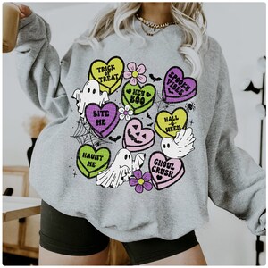 May include: Gray sweatshirt with a Halloween-themed design featuring candy hearts with phrases like "Trick or Treat", "Bite Me", and "Ghoul Crush".