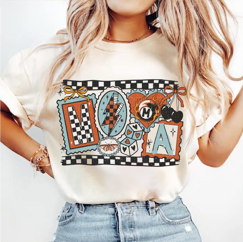 Op de afbeelding: Cr&egrave;mekleurig T-shirt met een retro grafisch ontwerp. Het ontwerp bevat de letters "M" en "A" in postzegelstijl frames, een bliksemschicht, dobbelstenen, een hart en kersen. Het shirt heeft een geblokte rand.