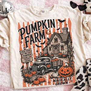 Peut inclure: Un t-shirt cr&egrave;me avec une impression graphique portant le texte PUMPKIN FARM et MAGICALLY GROWN. Le motif repr&eacute;sente une maison rustique, un vieux pick-up, un panneau en bois, des citrouilles, des chauves-souris et un croissant de lune.