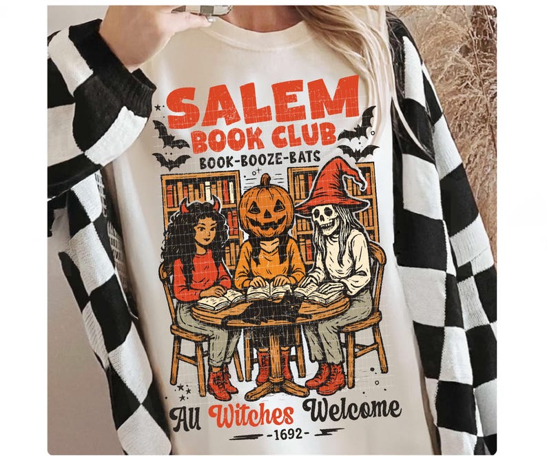 Może przedstawiać: Kremowa bluza z nadrukiem z napisem "Salem Book Club" oraz ilustracjami czarownic i nietoperzy. Projekt zawiera postać z dyniową głową, szkielet i postać z rogami czytające książki wok&oacute;ł stołu. Obecne jest r&oacute;wnież zdanie "All Witches Welcome - 1692".