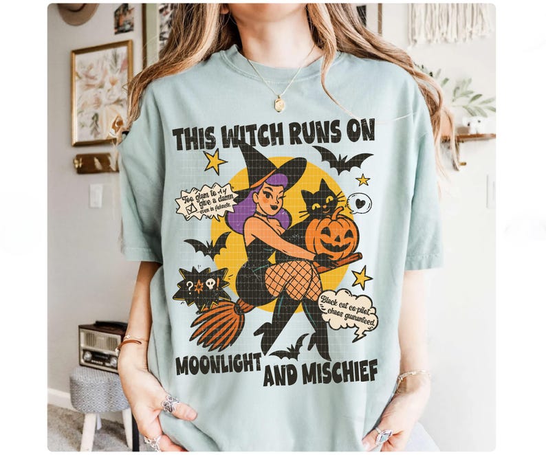 May include: A pale blue t-shirt with a Halloween graphic. The design shows a witch on a broom with a black cat and a pumpkin. The text on the shirt says "This Witch Runs On Moonlight And Mischief".