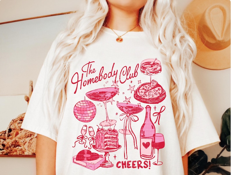 May include: White t-shirt with a pink graphic design that says "The Homebody Club" and features illustrations of a disco ball, champagne flutes, a bottle of wine, a glass of wine, a slice of pizza, and a cake. The text "CHEERS!" is at the bottom of the design.