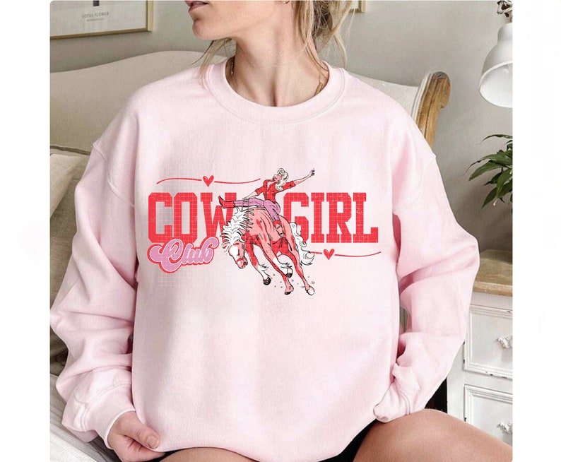 May include: Pink sweatshirt featuring a graphic of a woman riding a horse and the text "Cowgirl Club" in red.