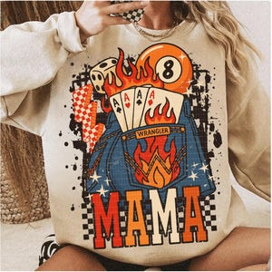 Può includere: Felpa beige con un design grafico raffigurante una palla 8, carte da gioco, dadi e fiamme. Il design include la parola "MAMA" a lettere grandi e un design a tasca in denim.
