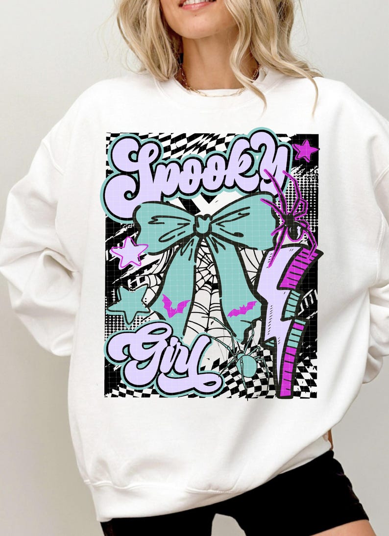 May include: White sweatshirt with a colorful graphic that says "Spooky Girl." The design includes a large teal bow, bats, stars, a spider, and a lightning bolt. The background has a black and white checkered pattern.