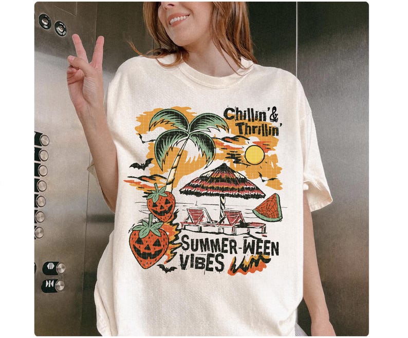 May include: Cream-colored t-shirt with a colorful graphic featuring a palm tree, sun, beach umbrella, and watermelon slice. The text reads "Chillin' & Thrillin'" and "Summer-ween Vibes". The design includes bats and jack-o'-lantern strawberries.