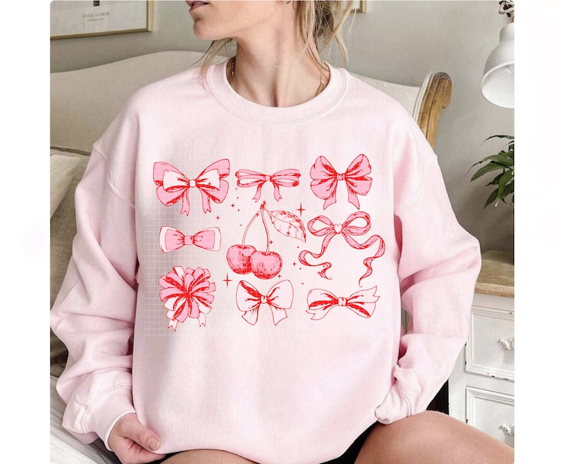May include: Pink sweatshirt with a graphic design of red bows, cherries, and stars.