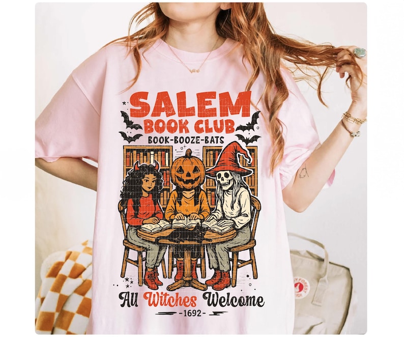 Może przedstawiać: Jasnor&oacute;żowa koszulka z napisem "Salem Book Club" i grafiką przedstawiającą trzy postacie wok&oacute;ł stołu. Postacie to wiedźma, dynia i szkielet. Tekst "All Witches Welcome - 1692" jest r&oacute;wnież zawarty.