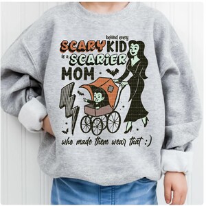 May include: A light gray sweatshirt with the text "behind every SCARY KID is a SCARIER MOM who made them wear that :)". The graphic includes a vampire in a stroller and a woman in a black dress.
