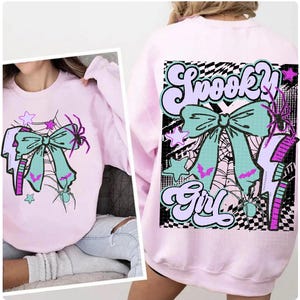May include: A light pink sweatshirt featuring a teal bow, spiderwebs, stars, and a lightning bolt graphic. The back of the sweatshirt has the words "Spooky Girl" in a retro font, with a bow, spider, and bat design.